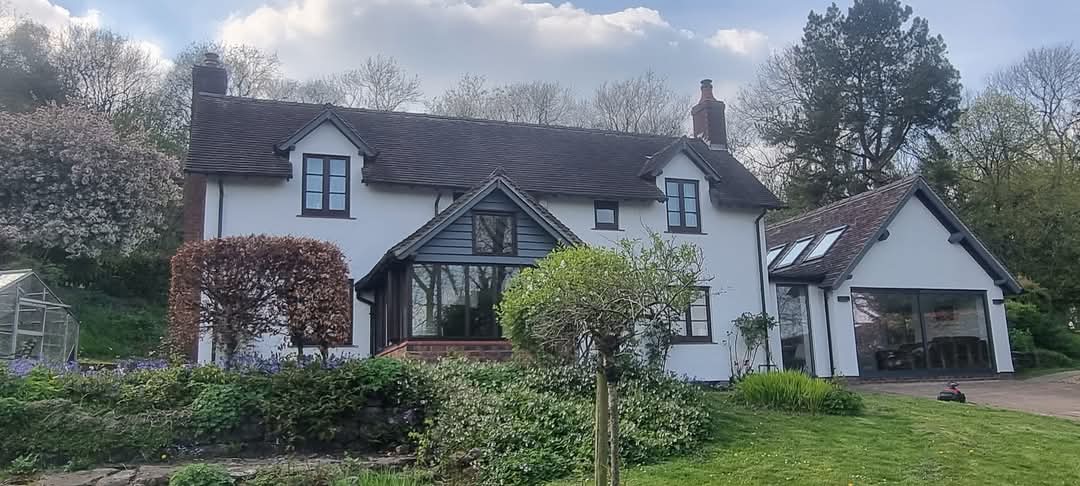A white-painted cottage with dark window frames behind a garden