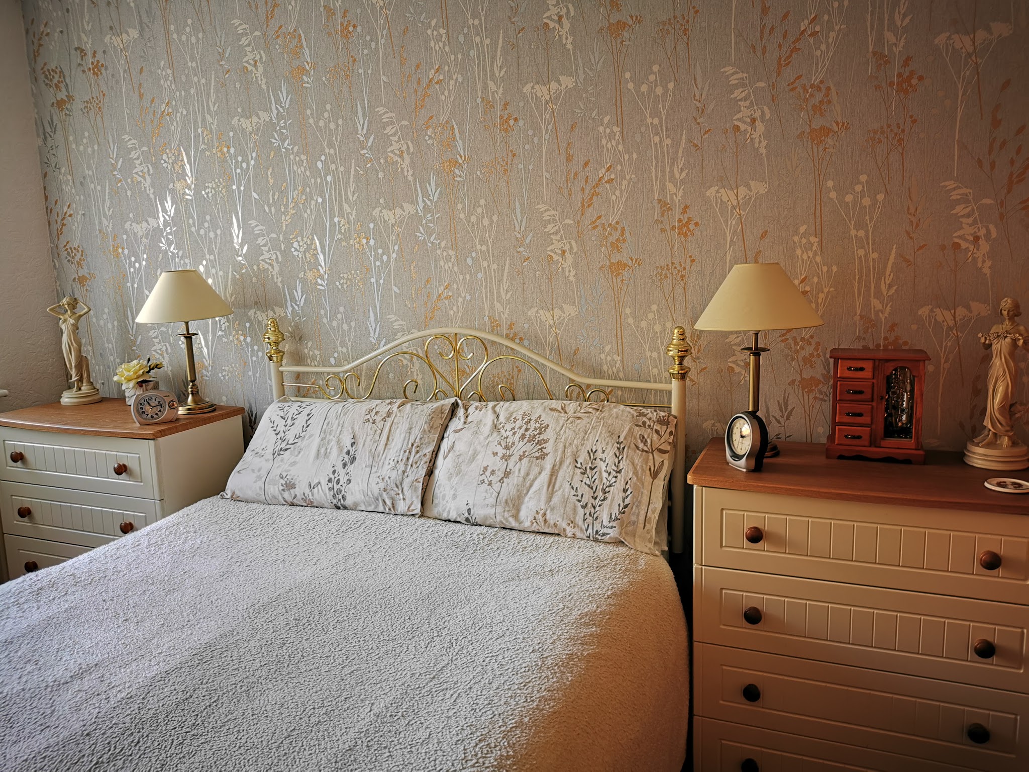 A bedroom with gold patterned wallpaper behind the bed