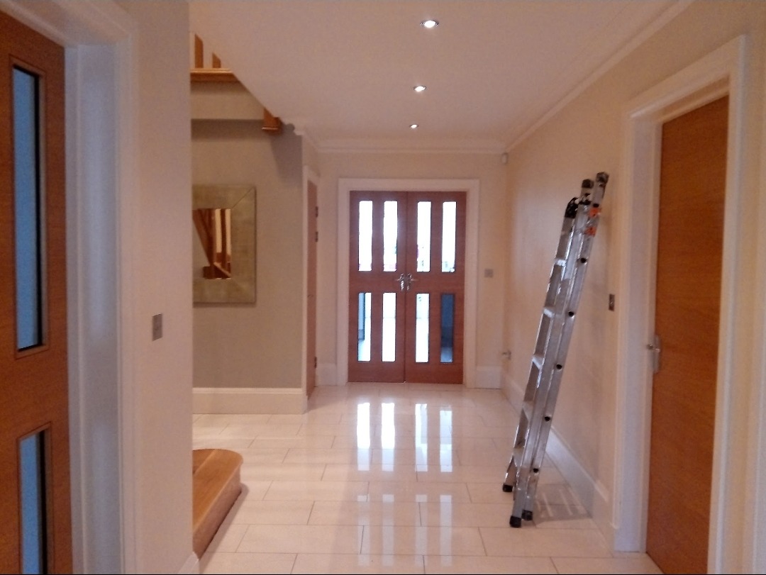 A long hallway with a glossy tiled floor, oak doors and a step ladder