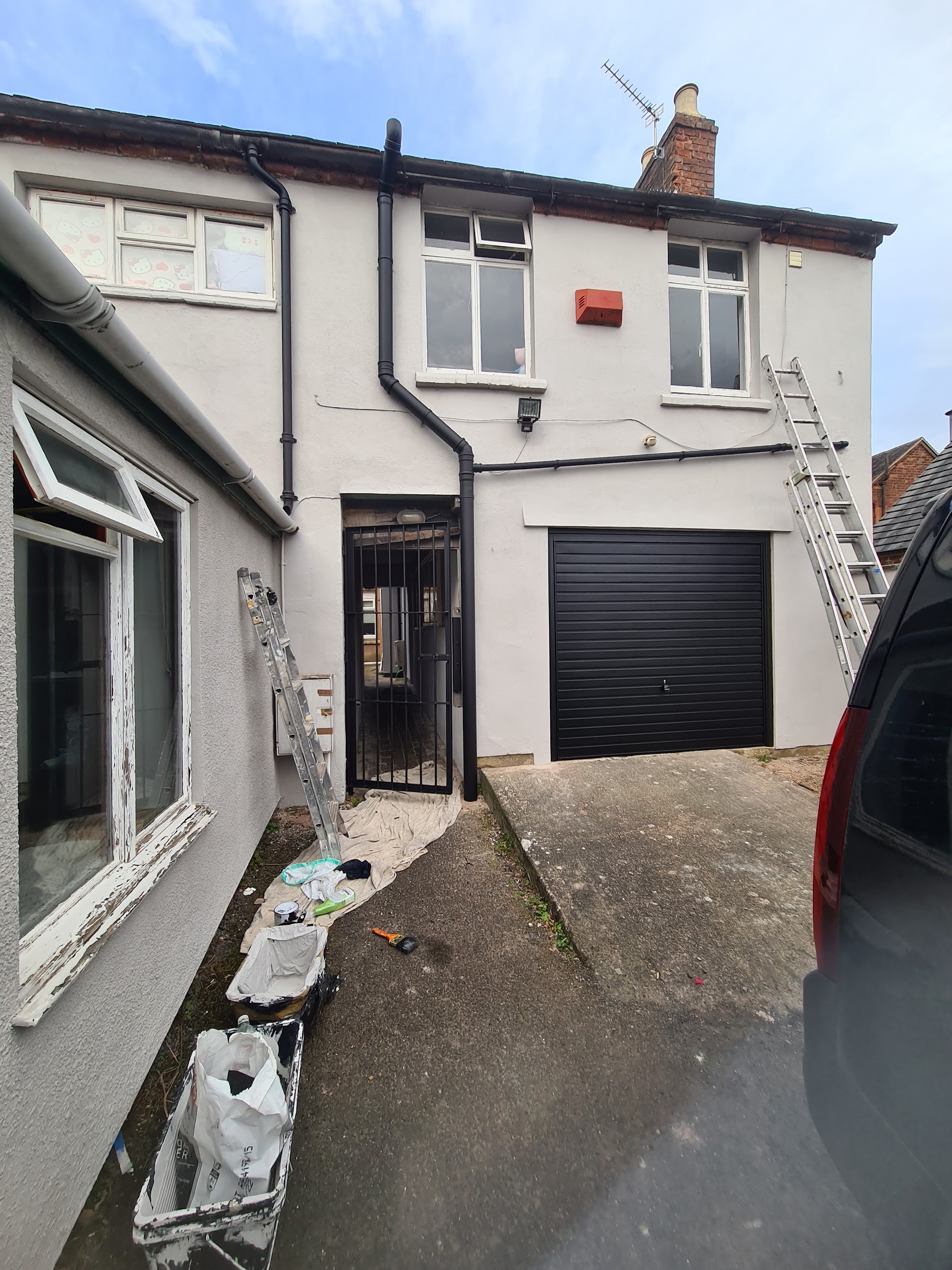 The rear of a white rendered house with ladders and a garage door