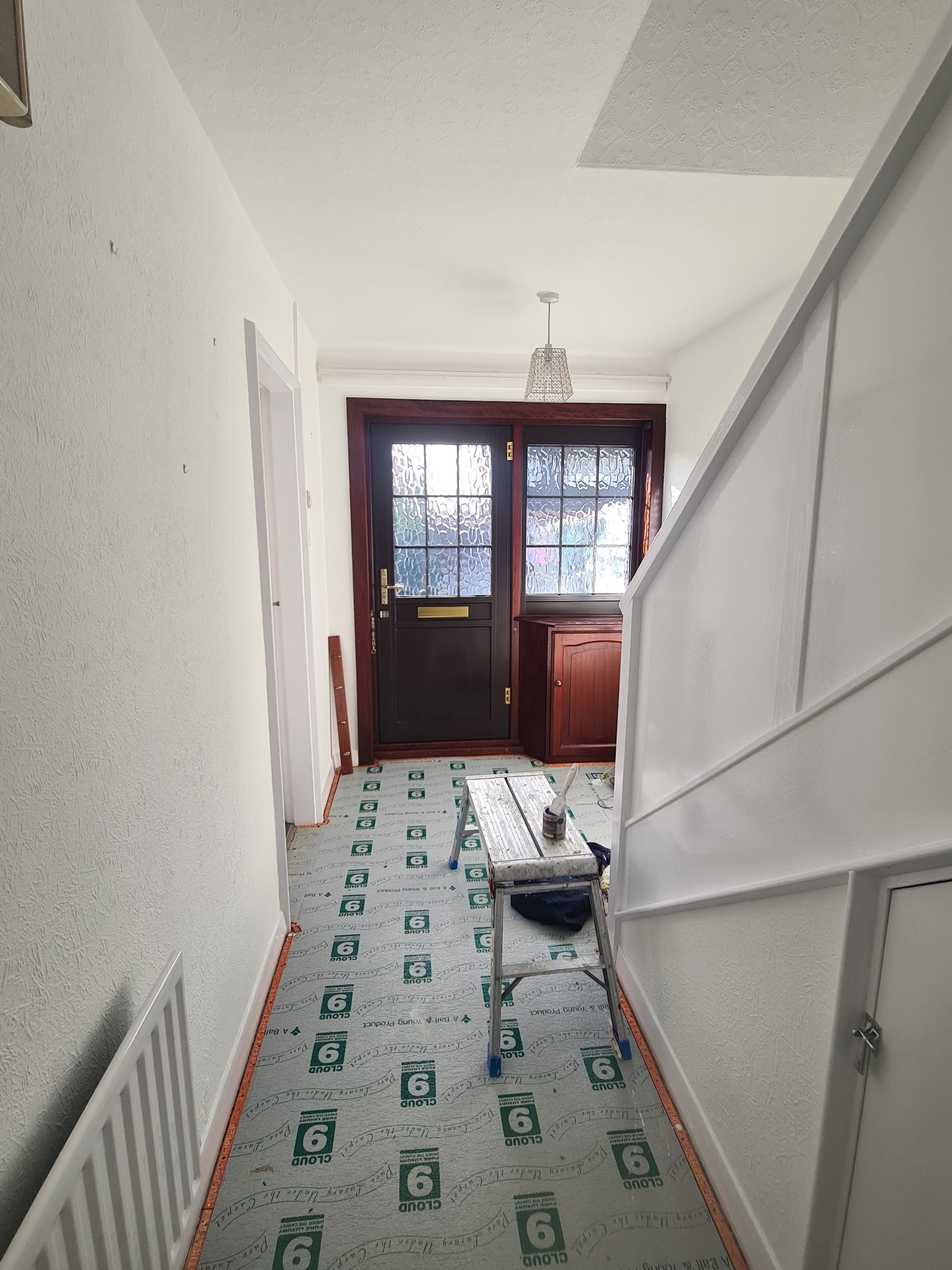 A white hallway with panelling and the front door, floor protection down
