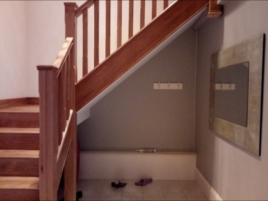 An oak staircase and banister above a freshly painted under-stairs wall